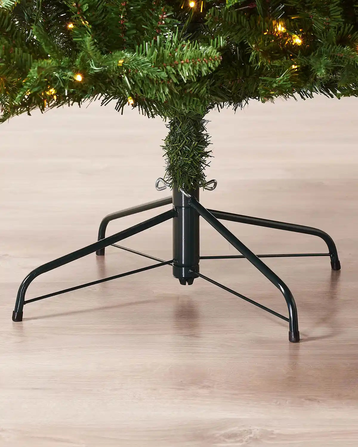Base detail of 8ft Grand Alaskan Fir Christmas tree showing dense lower green branches, warm white lights and sturdy support frame.