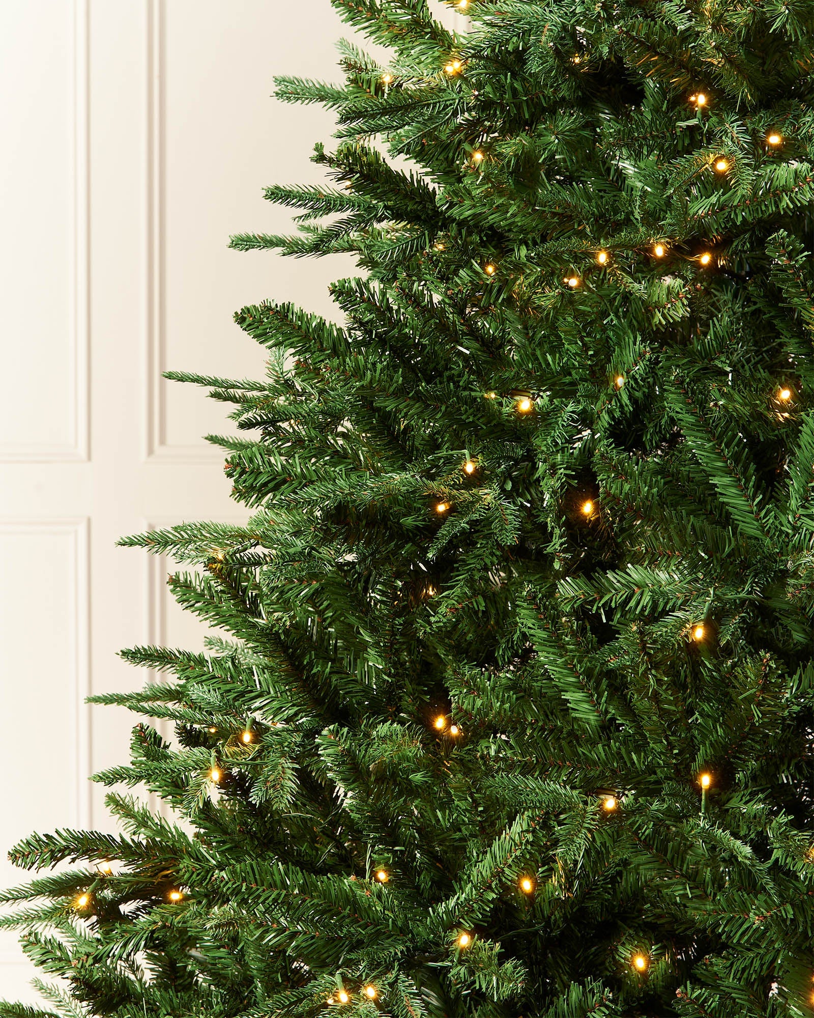 Close-up of layered green fir branches with warm white LED lights on a pre-lit Christmas tree