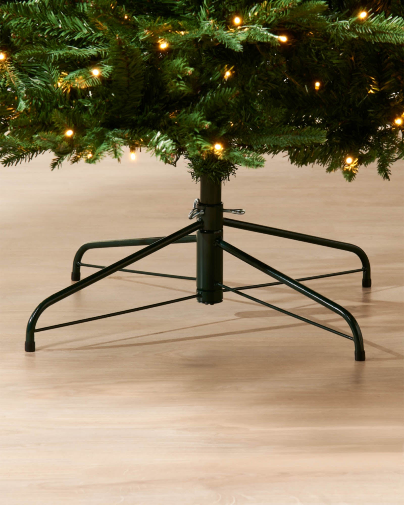Close-up of the base of a pre-lit green Christmas tree with warm white lights and a metal tree stand
