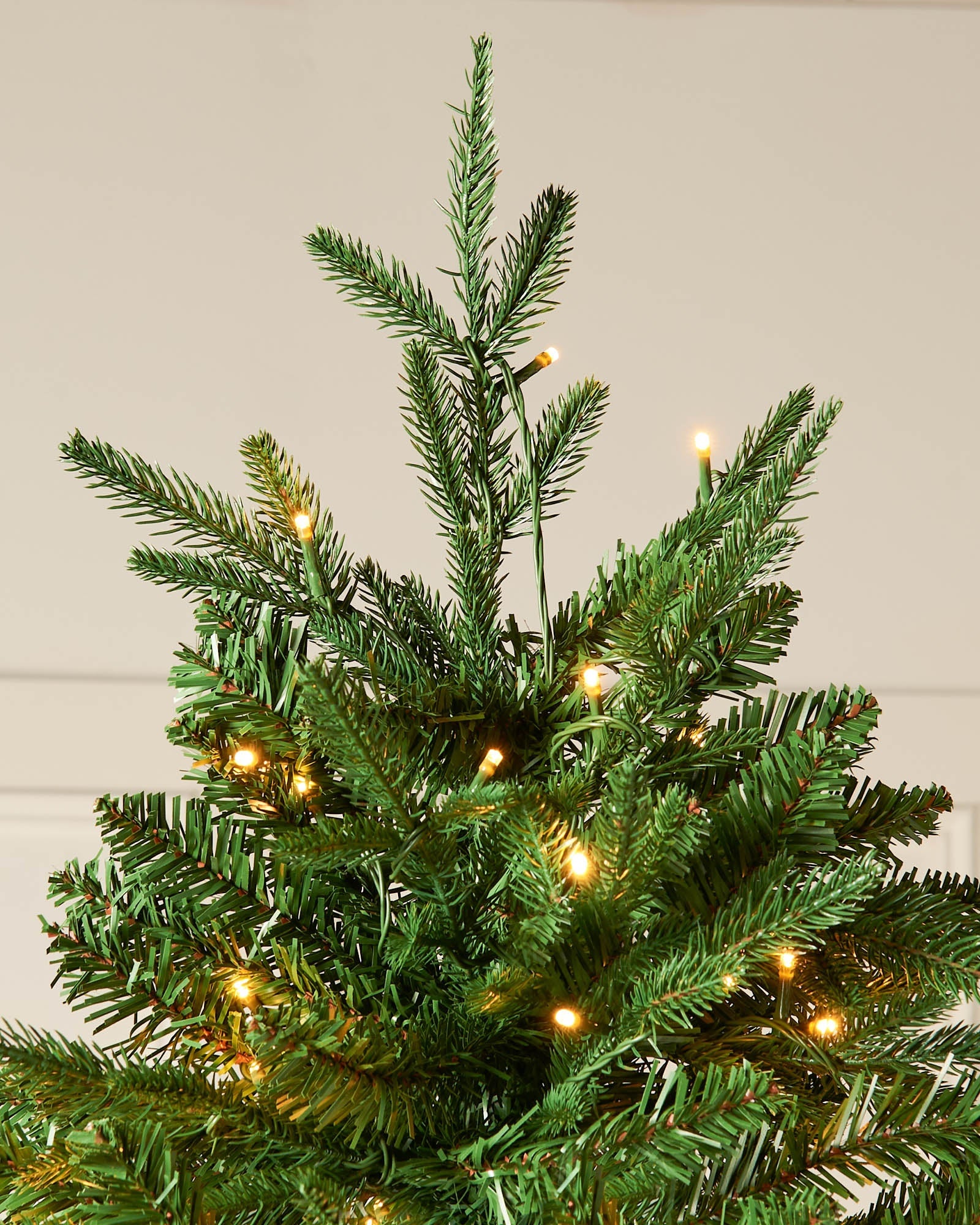 Top section of a pre-lit green Christmas tree with warm white LEDs and upright fir branches