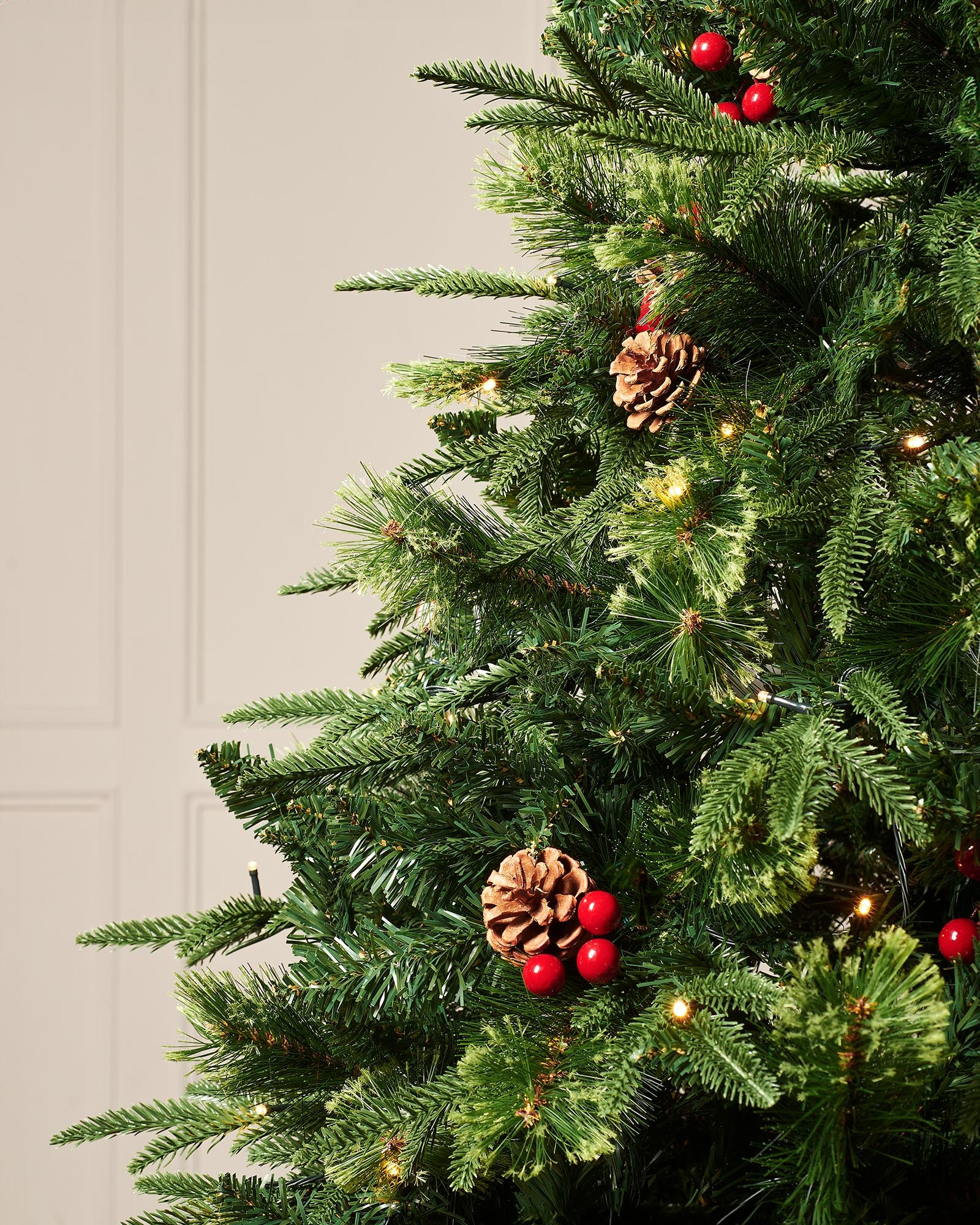 Close-up of the 8ft pre-lit Victorian Christmas tree showing mixed green branches, red berries, pinecones and warm white lights.