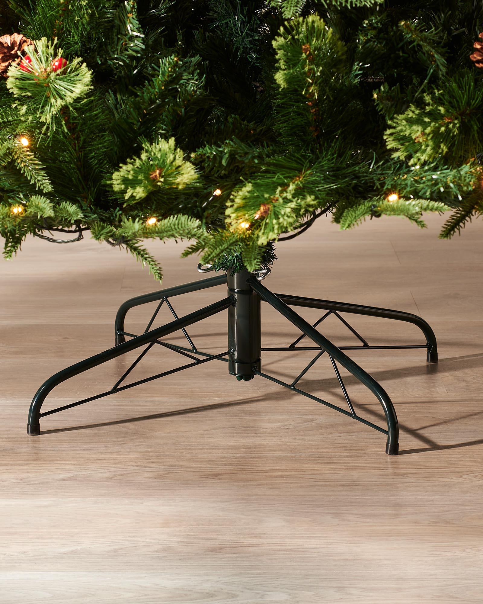 Close-up of the metal tree stand beneath the 8ft pre-lit Victorian Christmas tree on an indoor wooden floor.