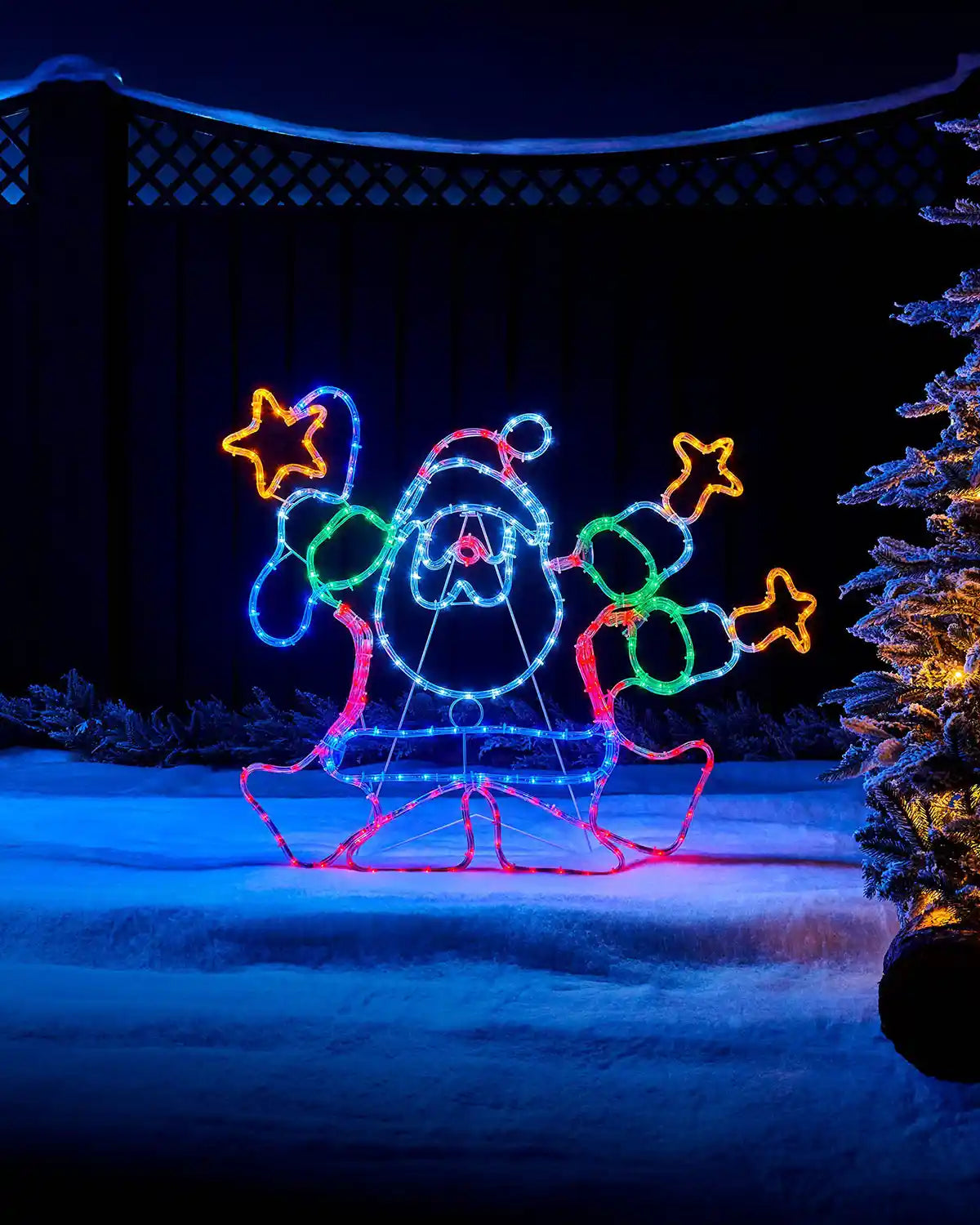Multi-coloured Santa rope light displayed outdoors beside a Christmas tree