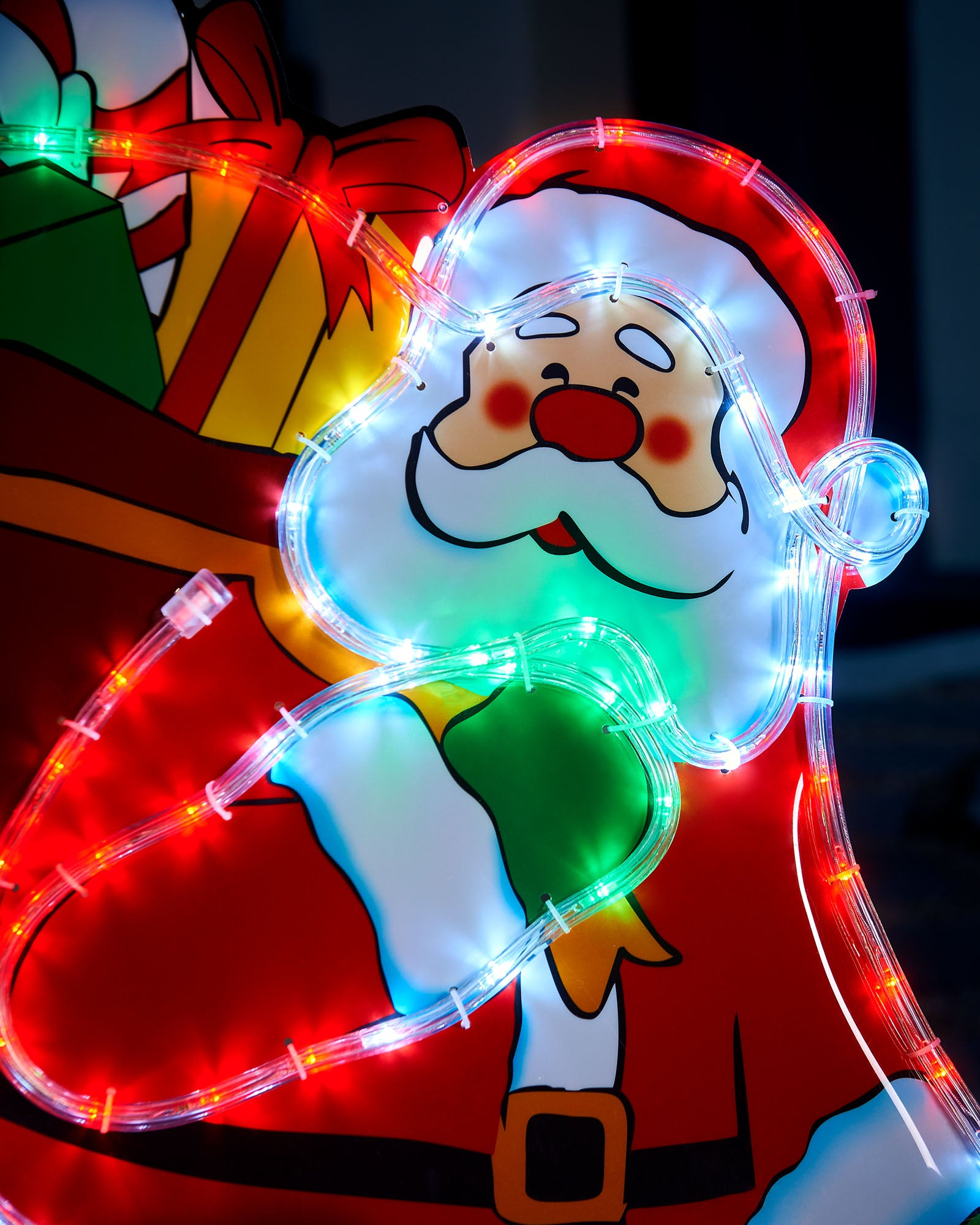 Close-up of Santa on chimney silhouette with illuminated face, gift sack and multi-coloured rope lights