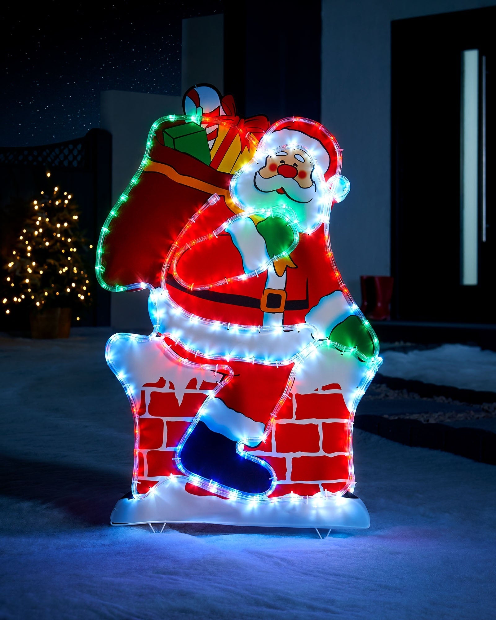 95 cm pre-lit Santa on chimney silhouette with multi-coloured LEDs in an outdoor Christmas display