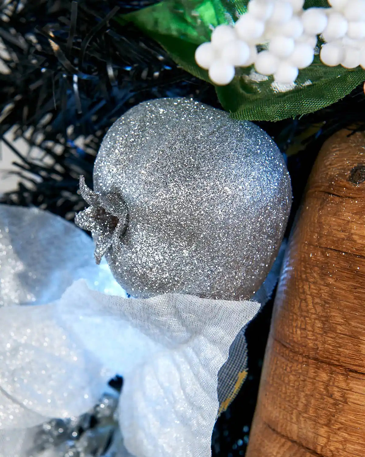 Detail close-up of silver glitter bauble, white poinsettia and black garland foliage