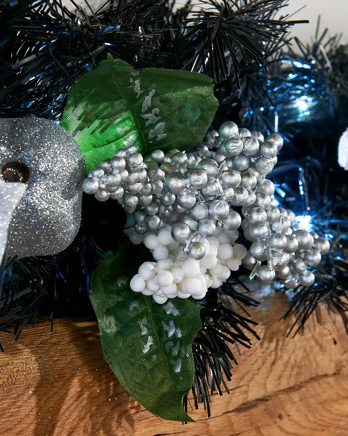 Detail close-up of silver and white berries, green leaves and cool white LEDs on a black Christmas garland