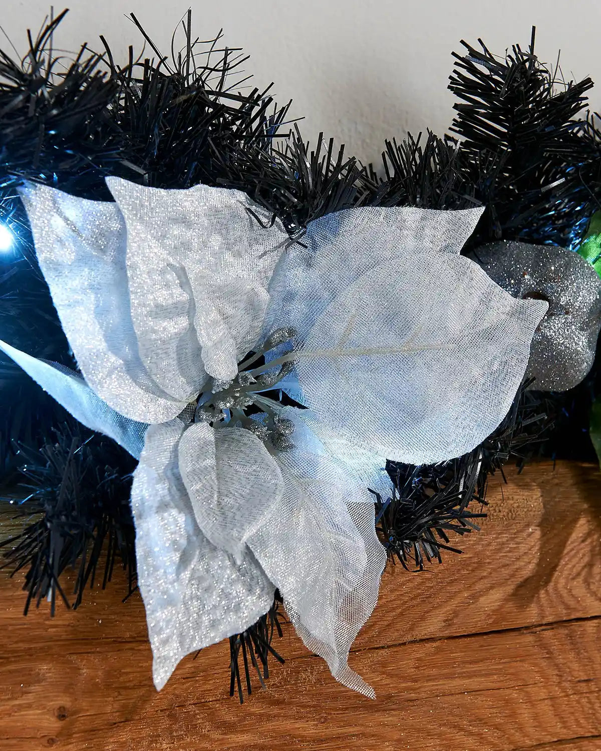 Close-up of white poinsettia, silver bauble and cool white lights on a black and silver Christmas garland