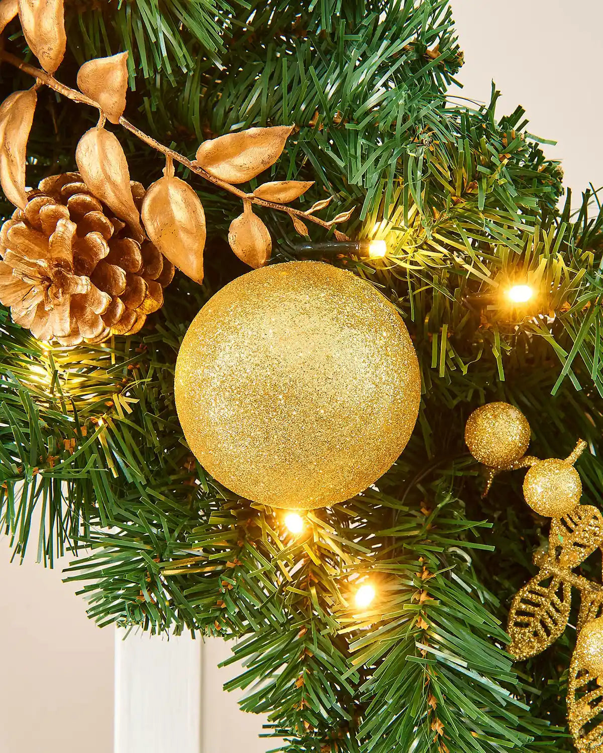Close-up of gold bauble, pinecone, metallic leaves and warm white LED lights on a Christmas garland