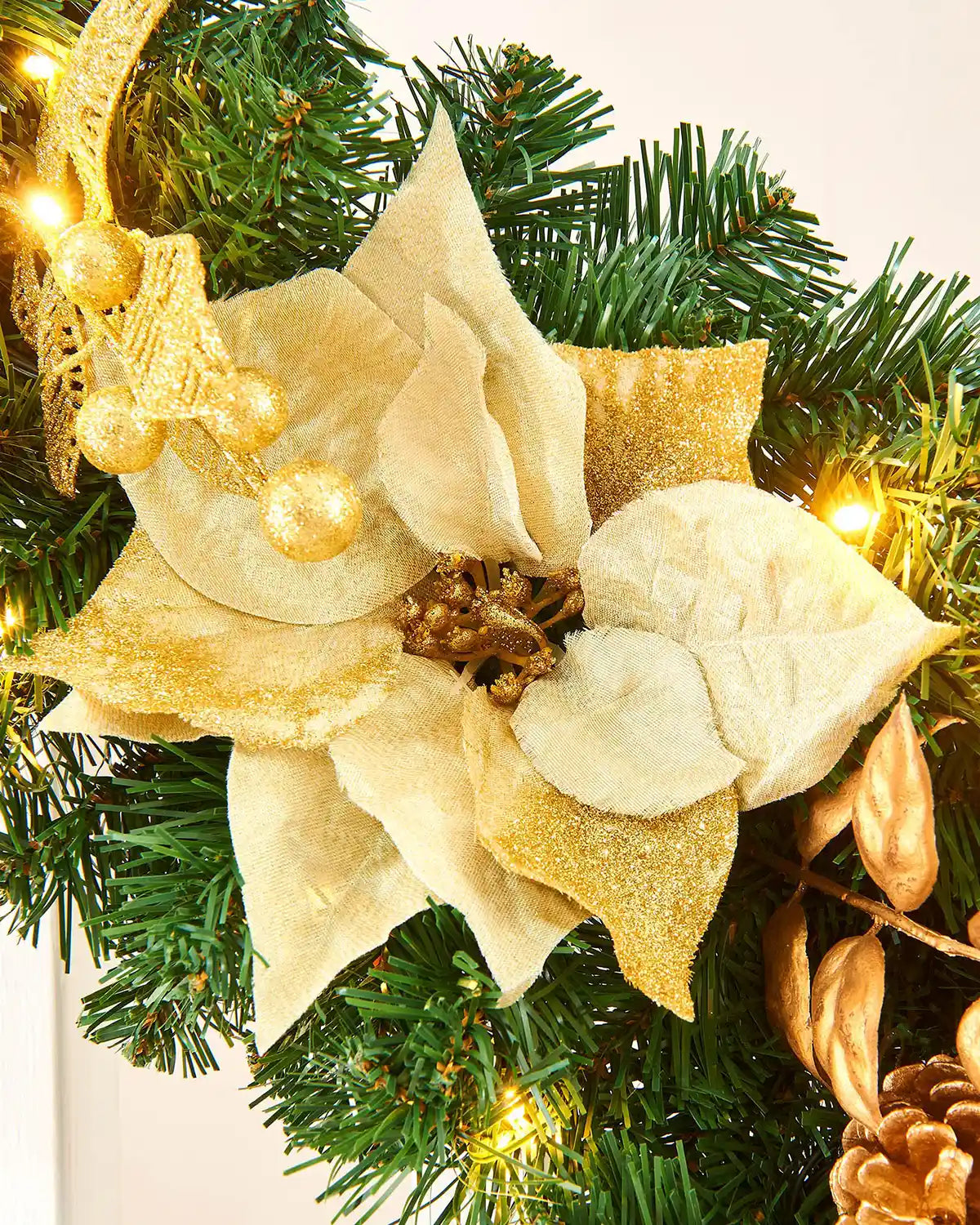 Detail close-up of cream poinsettia, gold leaves and warm white LEDs on a decorated Christmas garland