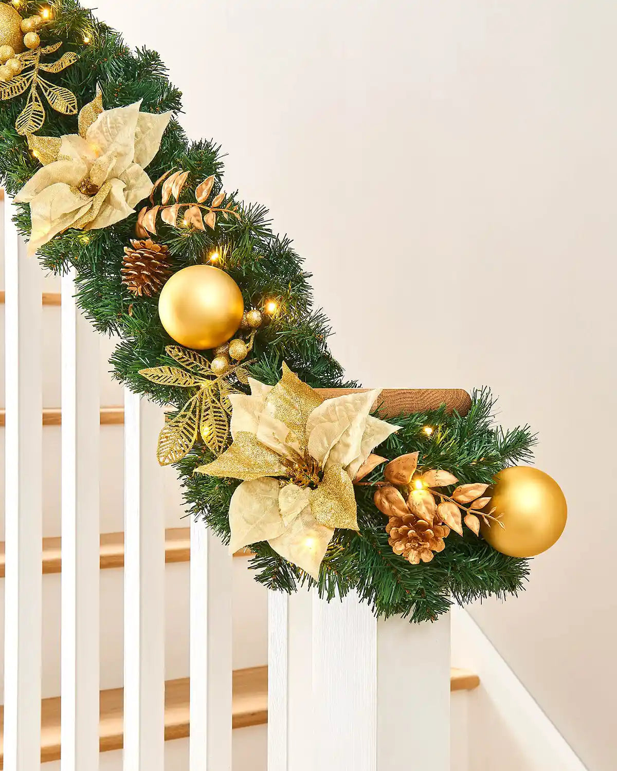 Detail of cream and gold decorated Christmas garland on a staircase with poinsettias, baubles, pinecones and warm white lights