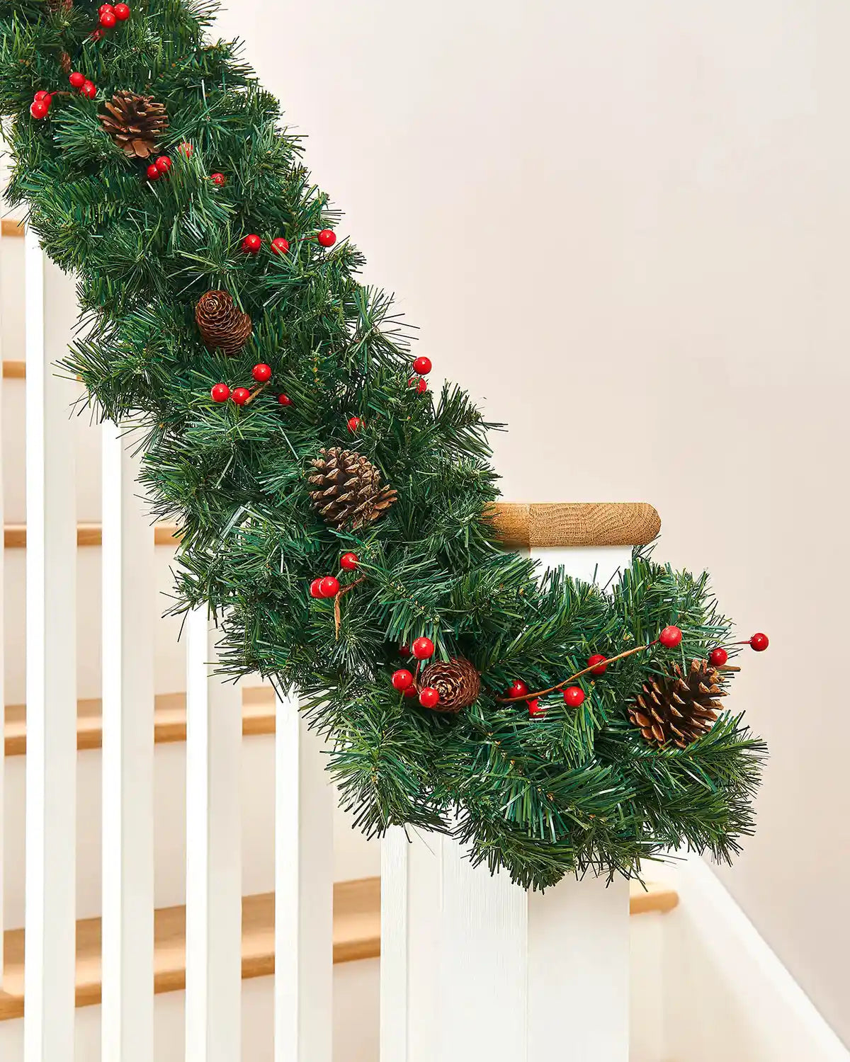 Green mixed pine garland with red berries and pine cones wrapped along a staircase bannister