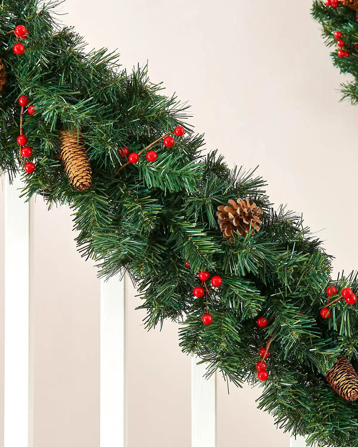 Close-up of a green mixed pine garland with red berries and natural pine cones on a staircase bannister