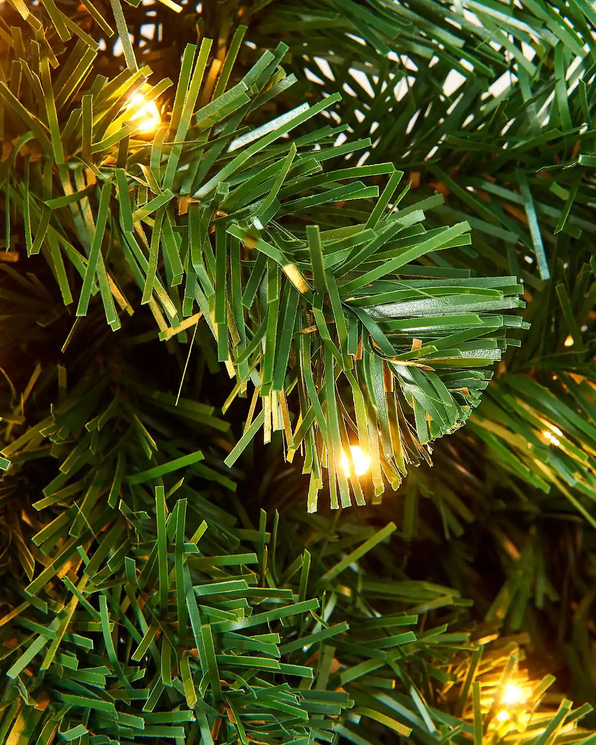 Close-up of green artificial pine garland branches with warm white LED lights