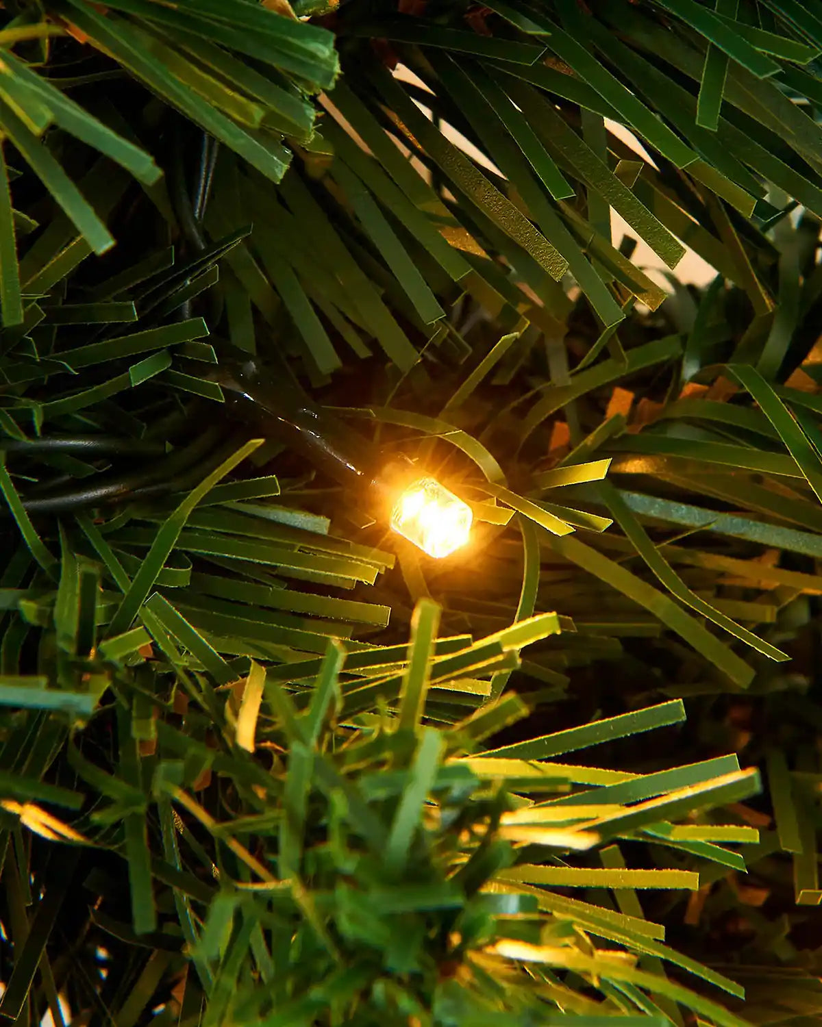 Detailed close-up of warm white LED light nestled among green pine garland foliage
