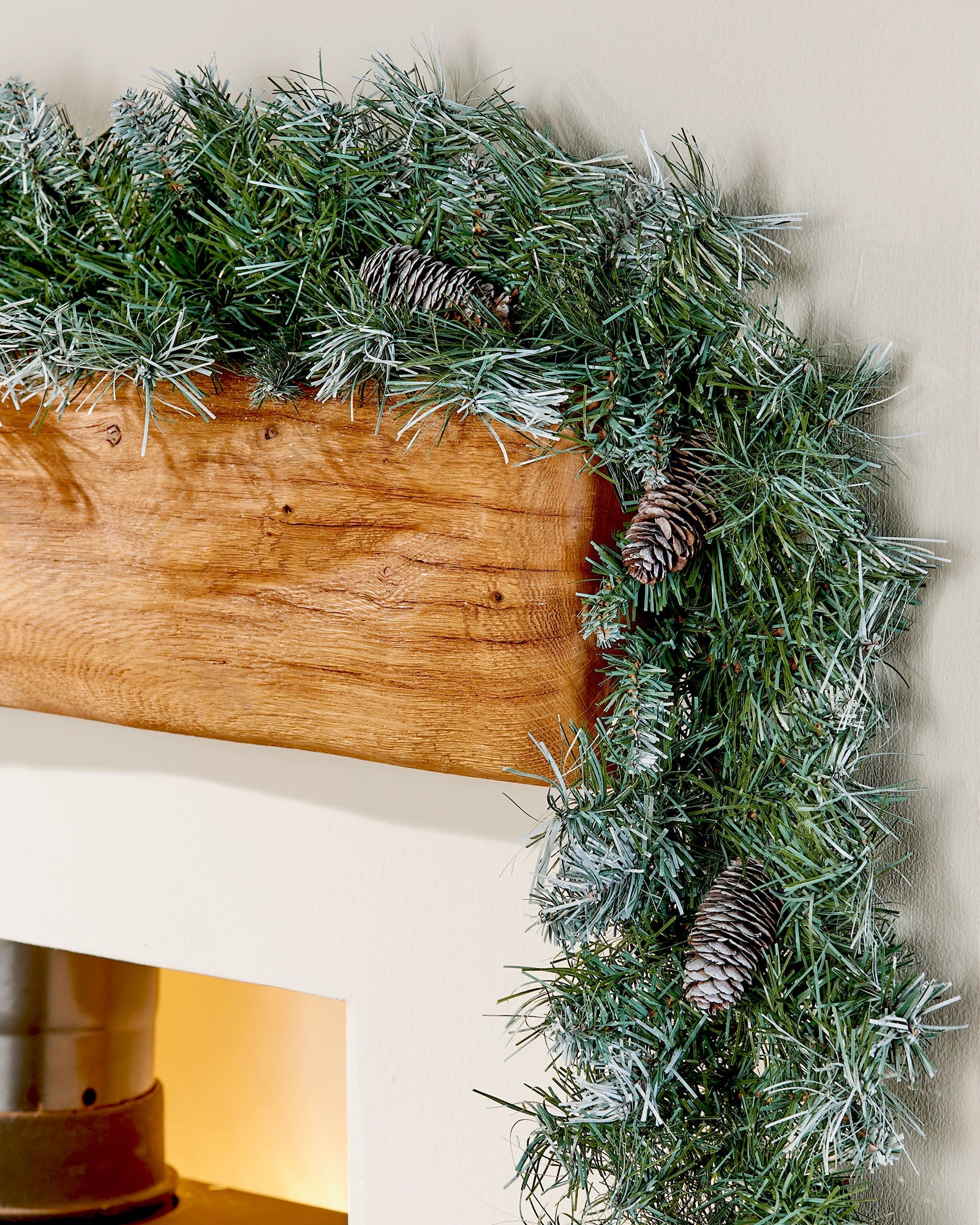 Close-up of a 9 ft frosted blue spruce garland with pinecones draped around a wooden mantelpiece