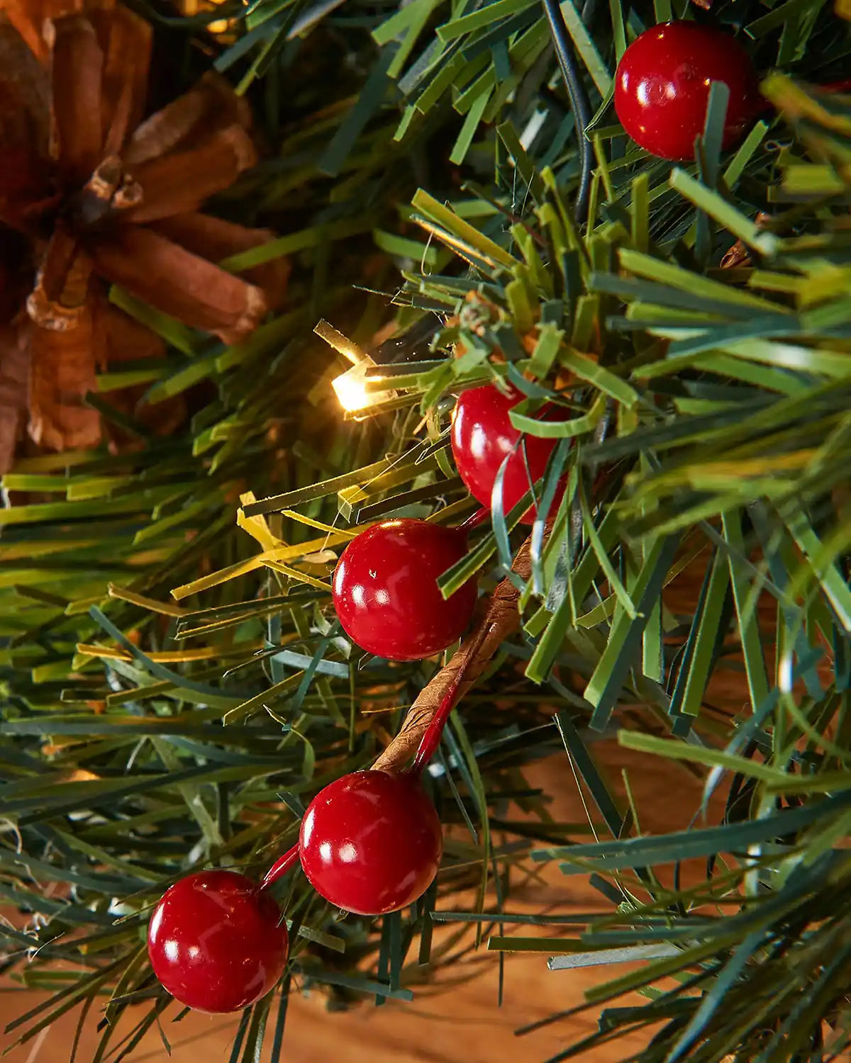 Detail close-up of red berries, green foliage and warm white LED lights on a Christmas garland