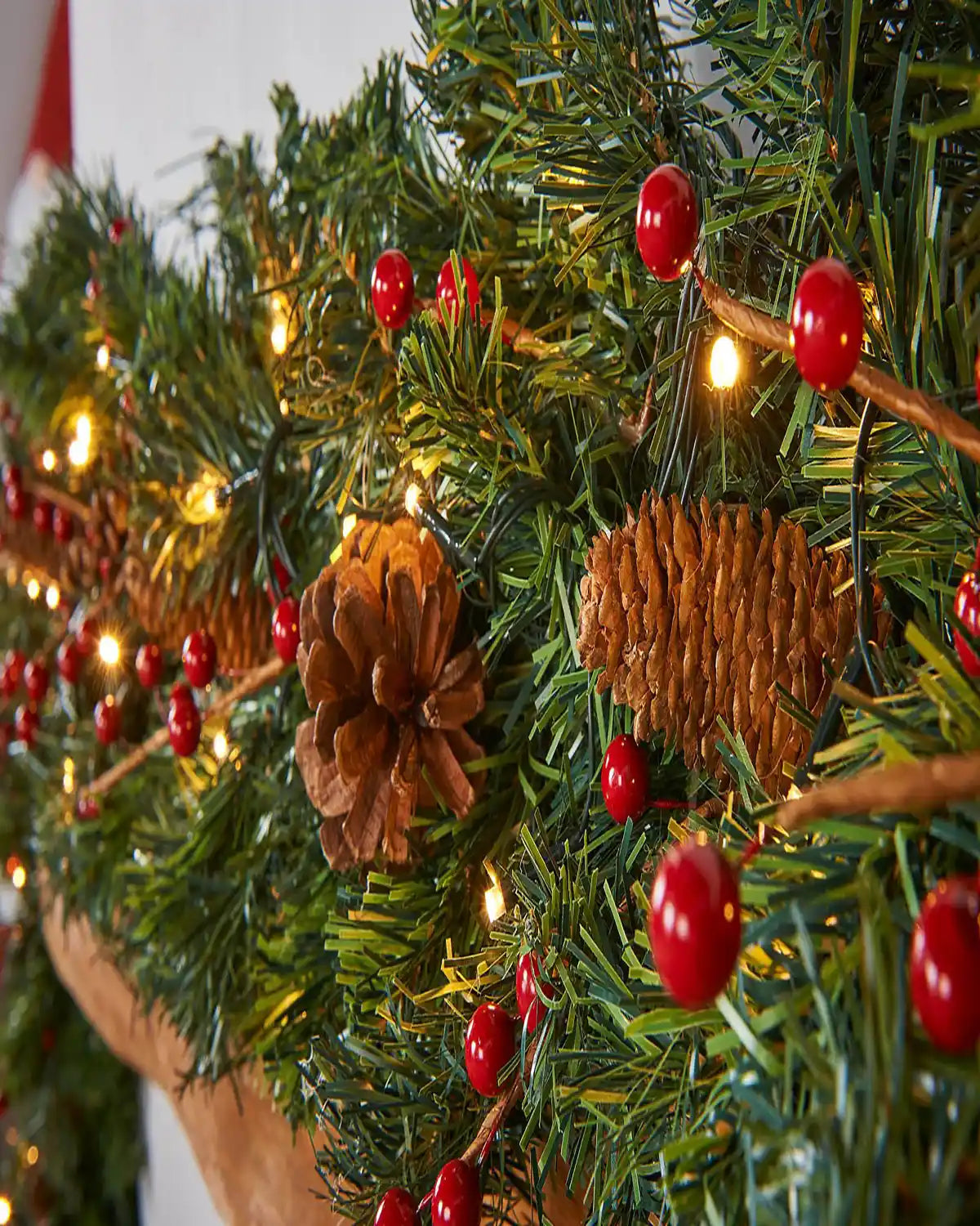 Close-up of Christmas garland with red berries, pinecones, green foliage and warm white LED lights