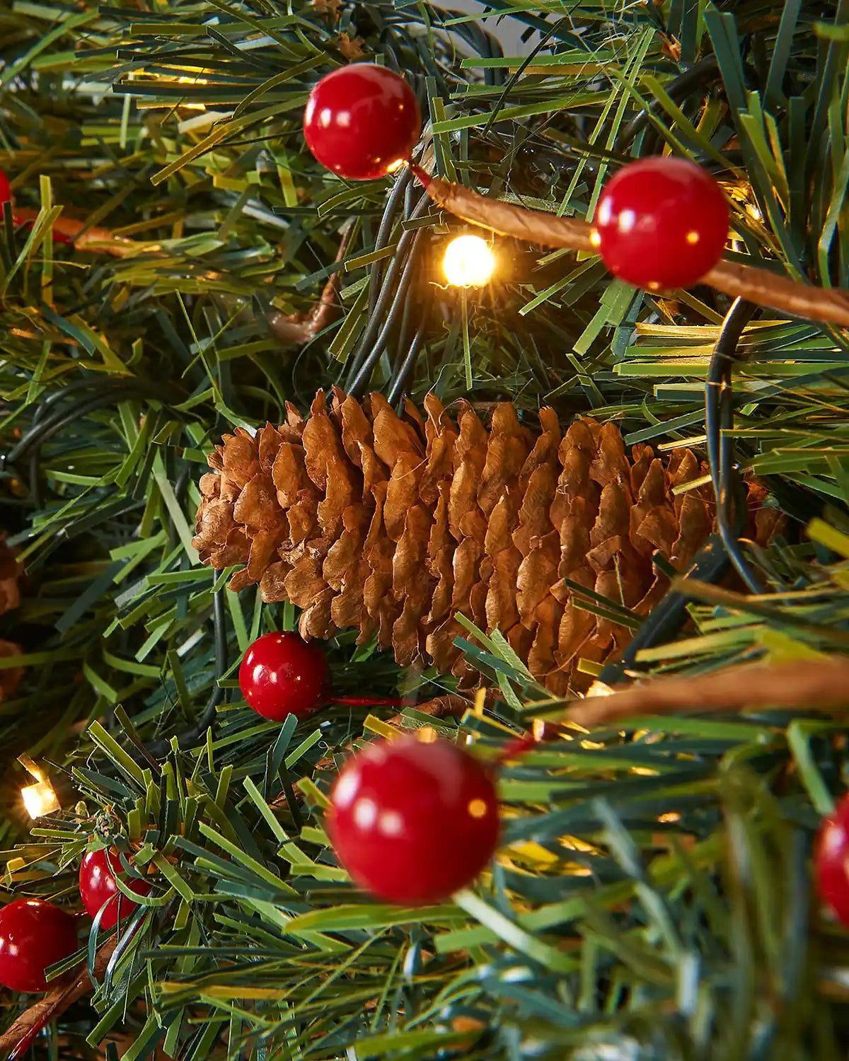 Close-up of warm white LED lights nestled among green artificial garland foliage and red berries
