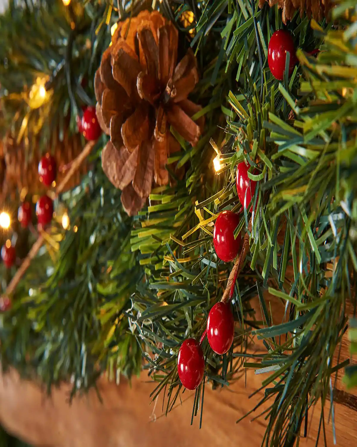 Detail close-up of pinecone, red berries and warm white lights on an extra thick Christmas garland
