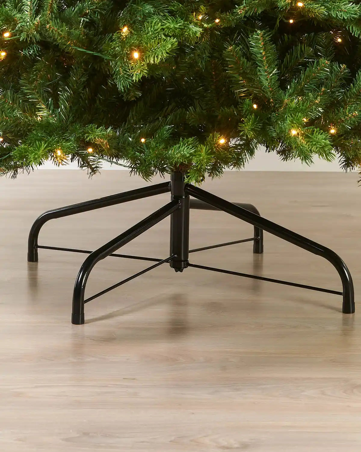 Close-up of the base of the 9ft pre-lit balsam fir Christmas tree showing the lower branches, warm white LED lights and metal tree stand.
