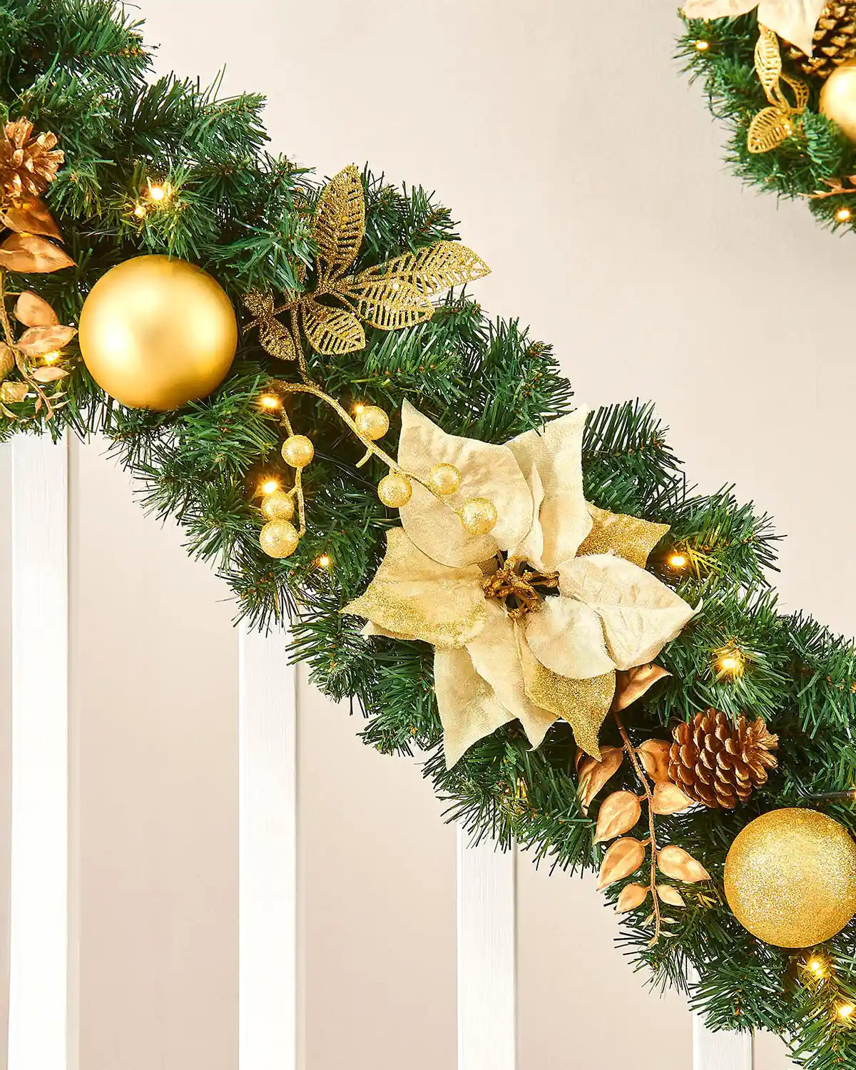Close-up of cream and gold decorated Christmas garland with poinsettia, gold bauble and warm white LED lights