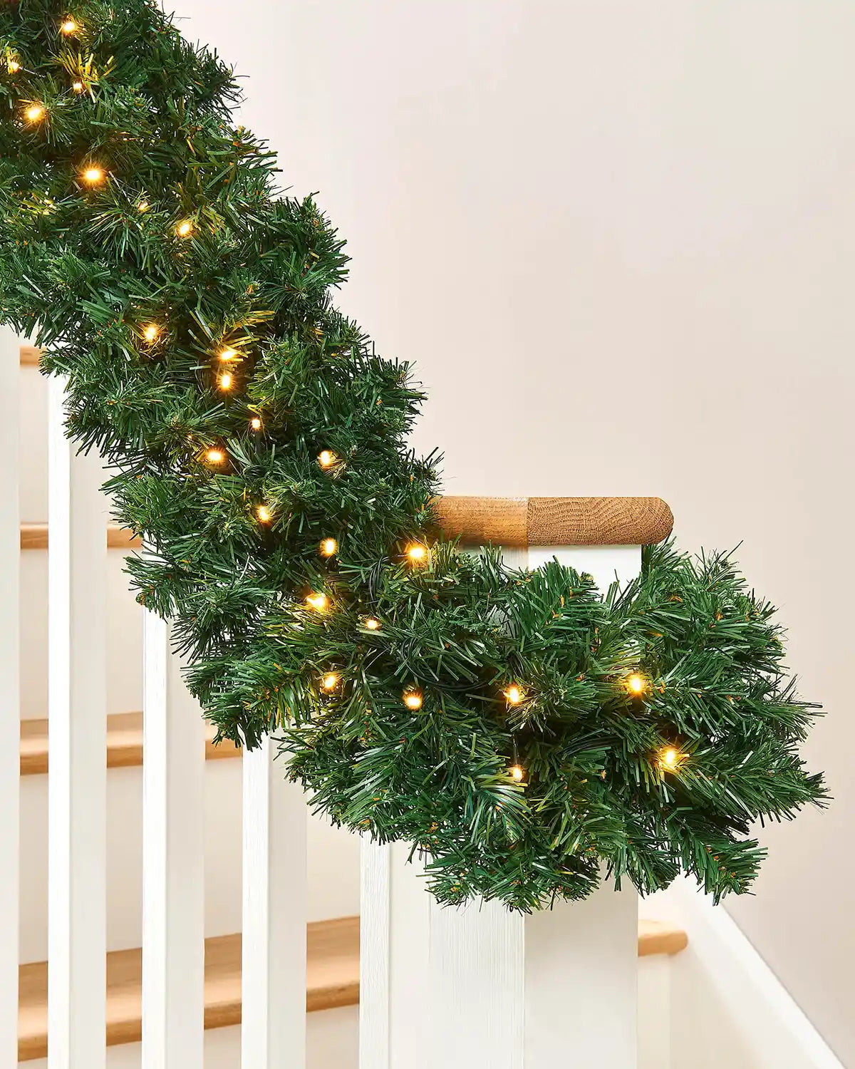 Detail of extra thick pine Christmas garland wrapped around a staircase banister with warm white lights