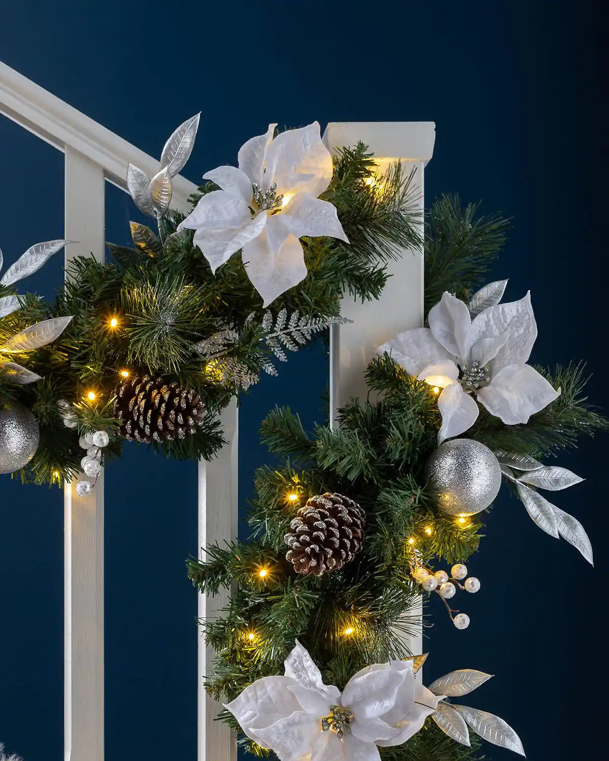 Extra thick silver and white pre-lit Christmas garland styled on a staircase with warm white lights