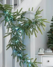 9ft pre-lit frosted fir garland with cool white lights draped around a white stair banister