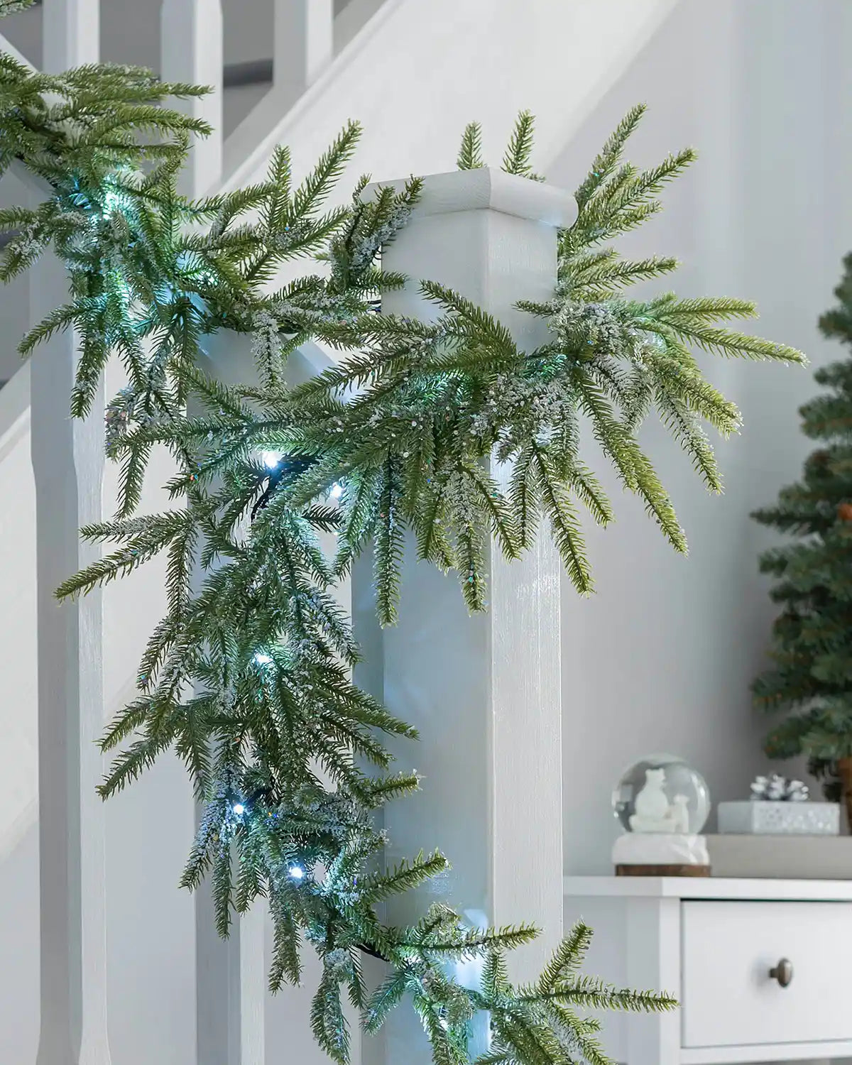 9ft pre-lit frosted fir garland with cool white lights draped around a white stair banister