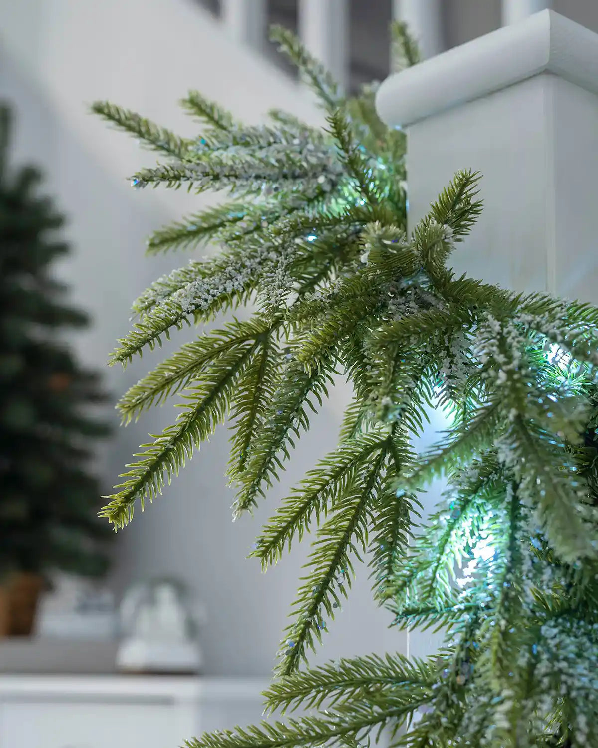 Close-up of frosted green fir branches with cool white lights on a stair banister