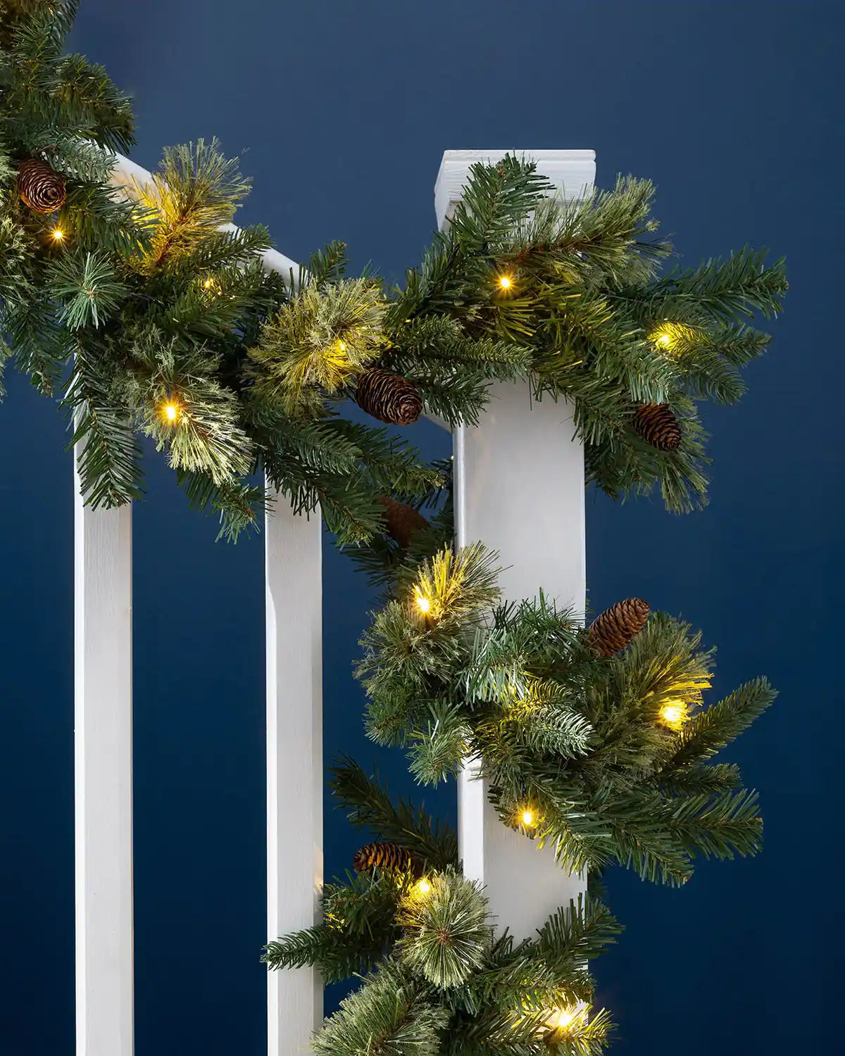 Pre-lit natural pine Christmas garland styled on a staircase with pinecones and warm white lights