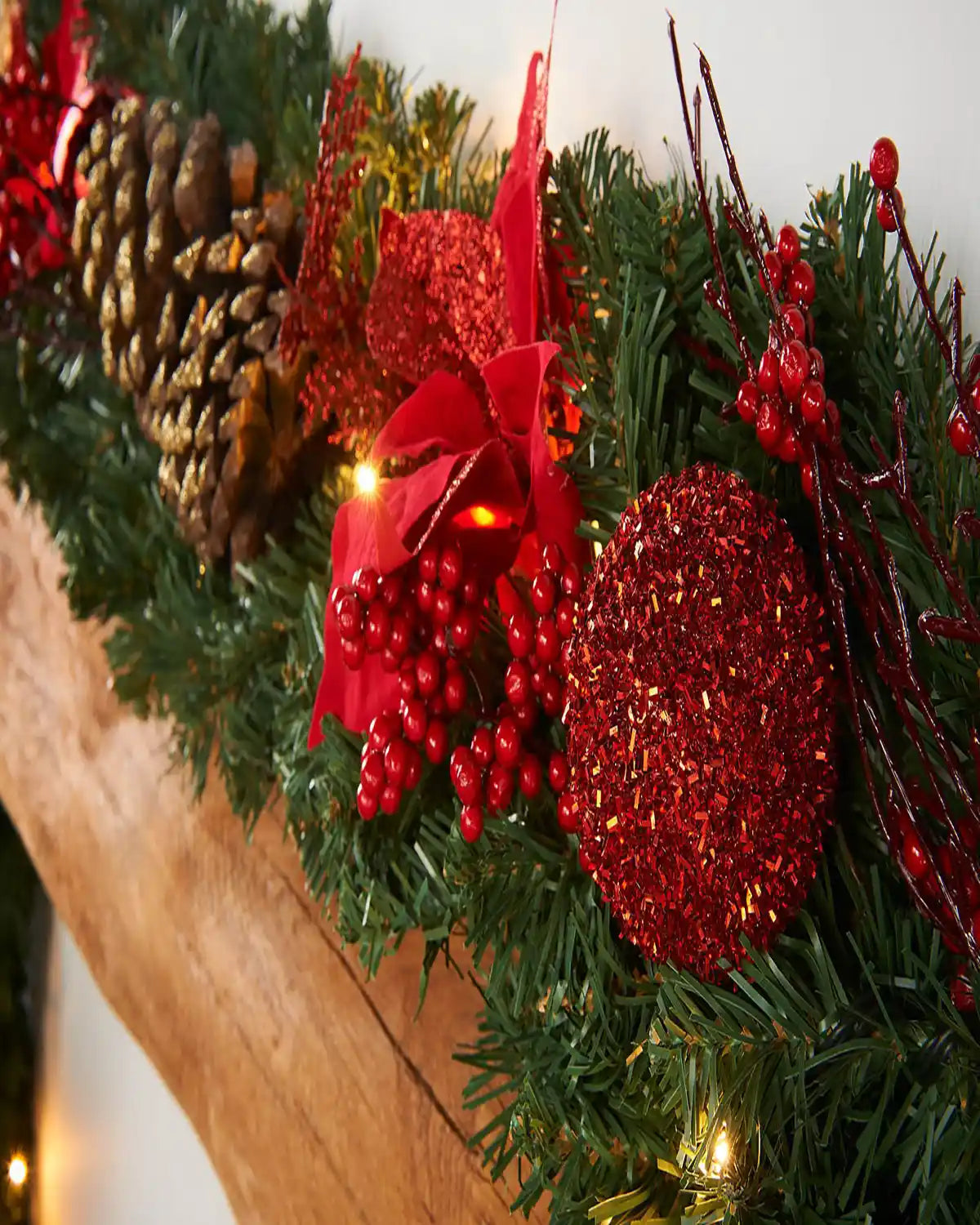 Close-up of a decorated garland with red berries, glittered red decoration, pine cone and warm white LED lights