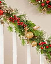 Close-up of a 9ft pre-lit mixed tip garland with red berries, gold baubles and green foliage on a staircase.