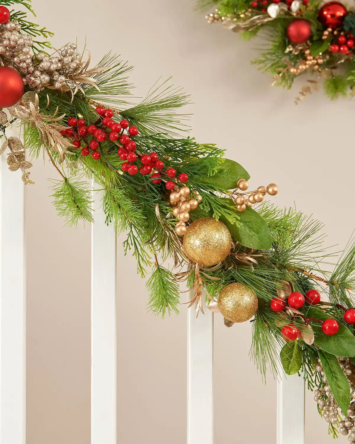 Close-up of a 9ft pre-lit mixed tip garland with red berries, gold baubles and green foliage on a staircase.