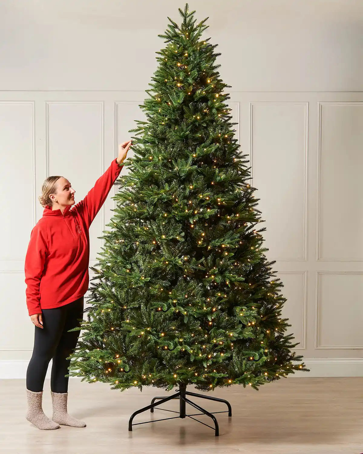 9ft pre-lit Royal Fir Christmas tree with warm white LEDs, shown indoors beside a person for scale.