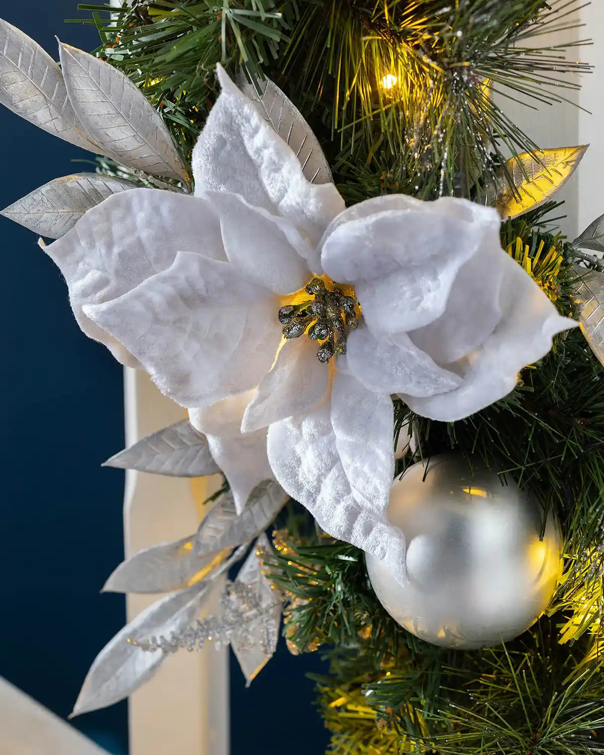 Close-up of a white poinsettia, silver bauble and warm white lights on the Christmas garland