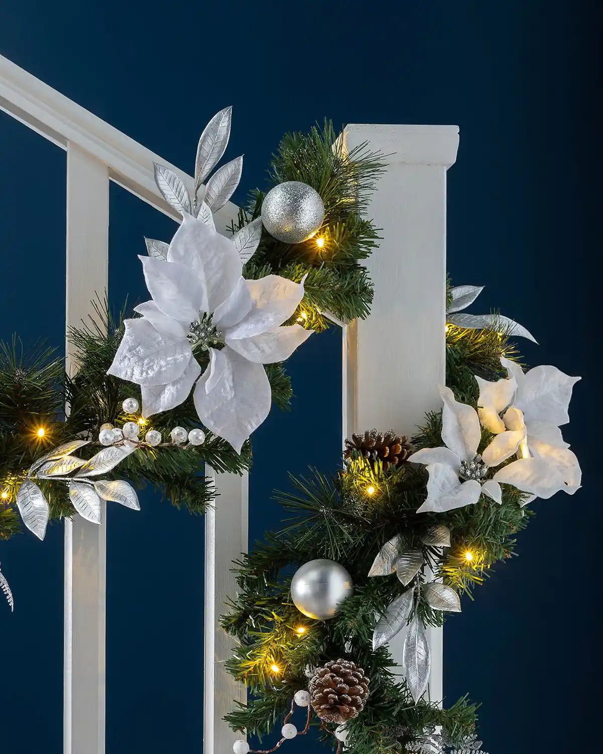 Silver and white pre-lit Christmas garland styled on a staircase with warm white lights