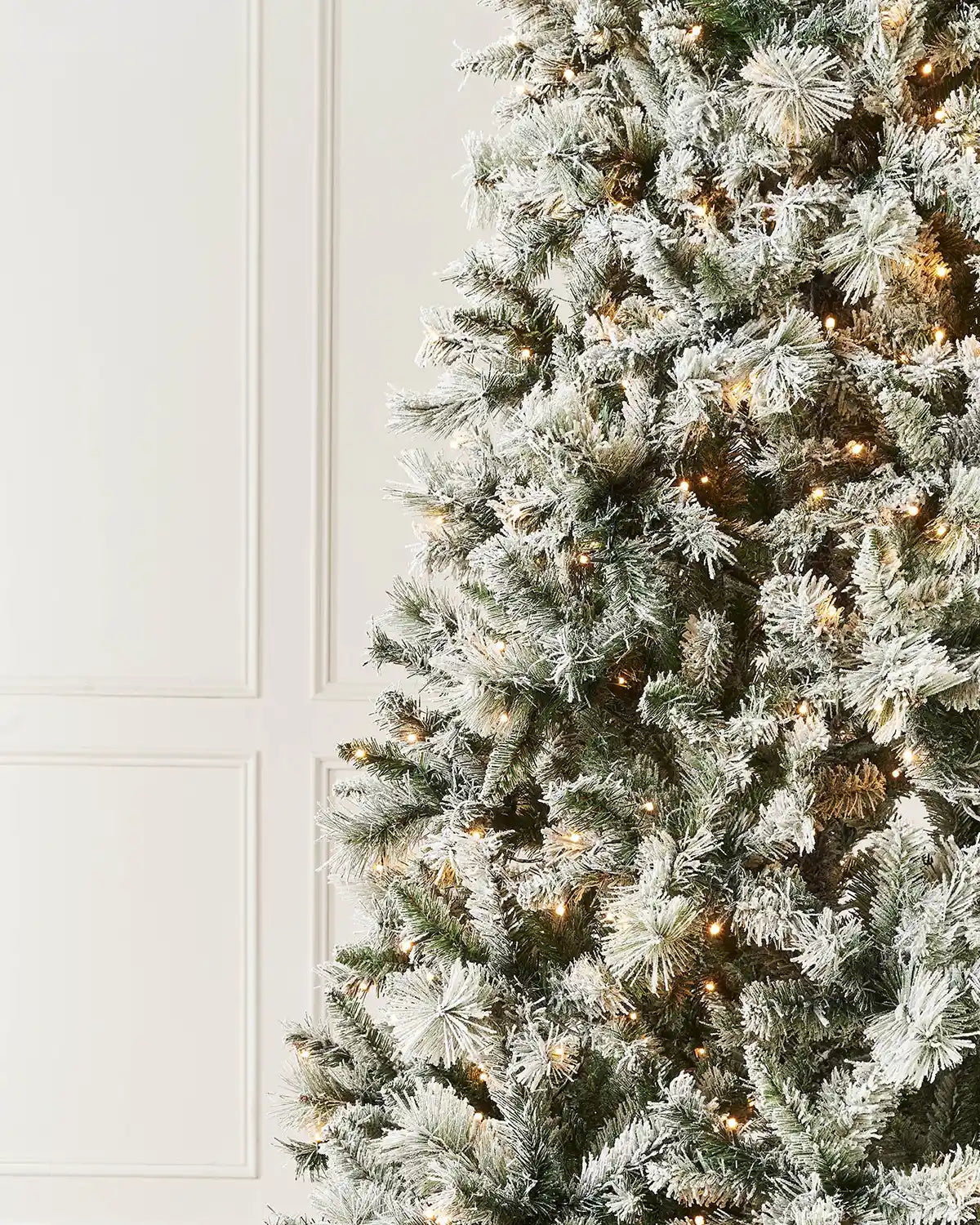 Close-up of snow flocked spruce branches with warm white lights and mixed green foliage.