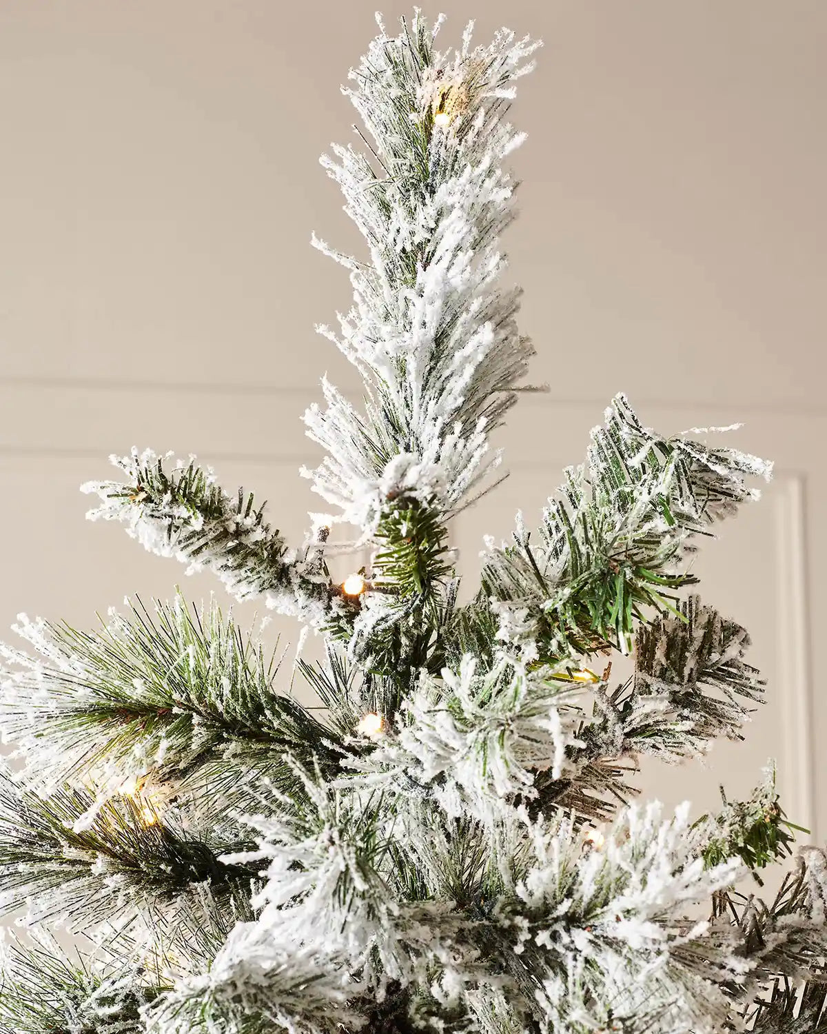 Top section of a 9 ft snow flocked spruce Christmas tree with warm white lights.