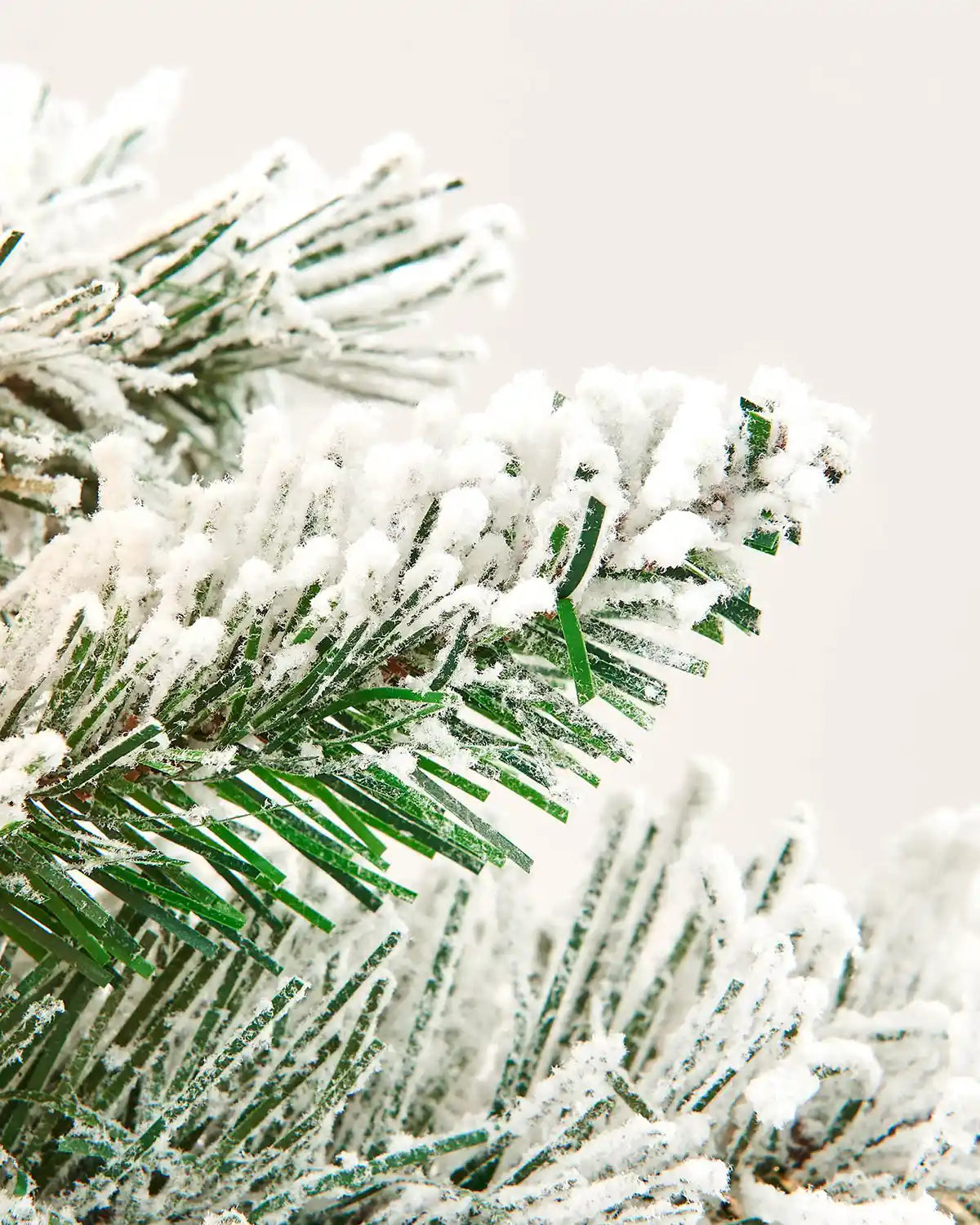 Close-up of green PVC spruce tips covered with artificial snow on a pre-lit garland