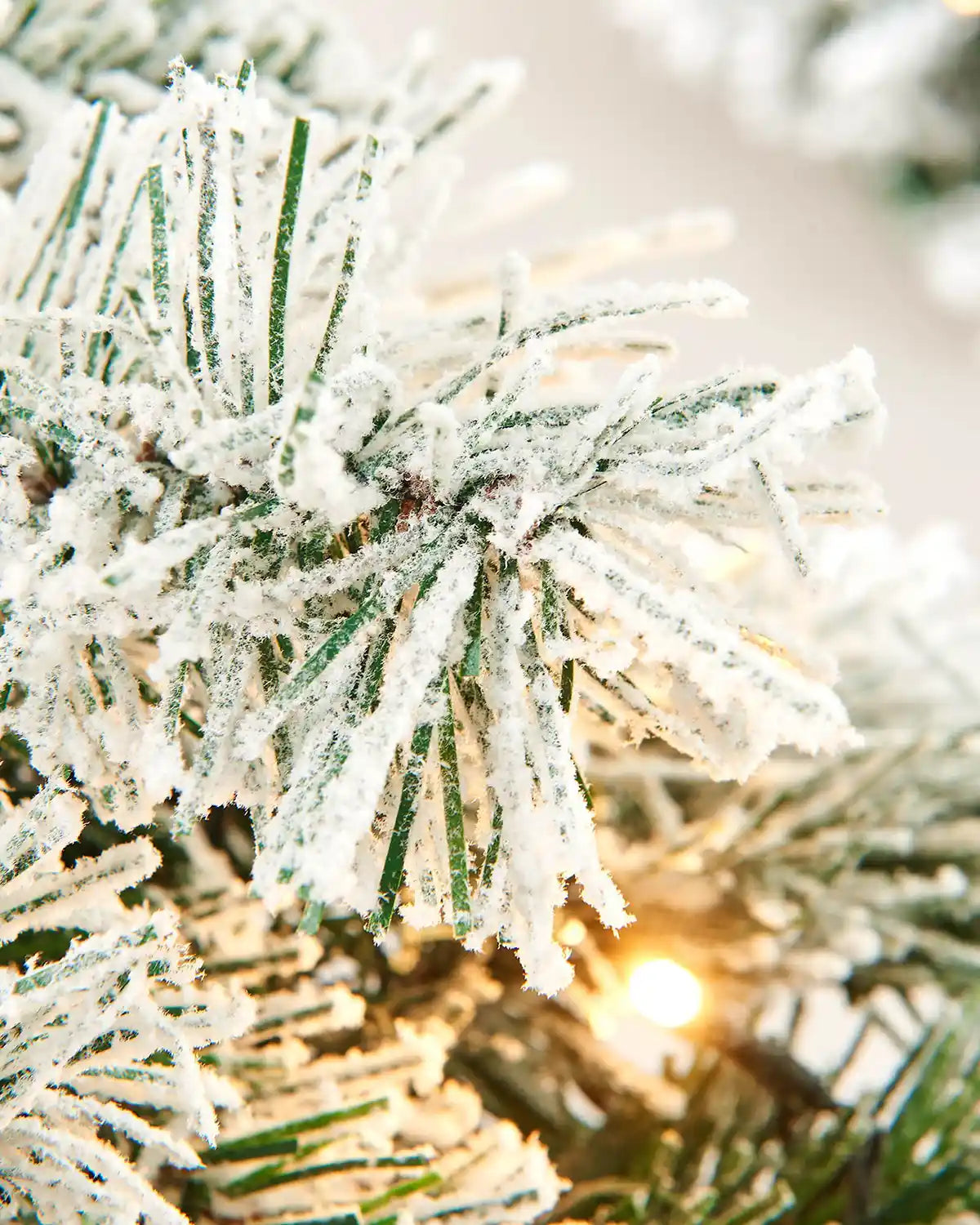 Close-up of snow-flocked spruce garland branches with a warm white LED light glowing between the tips