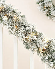 Close-up of a 9ft snow-flocked spruce garland with warm white lights wrapped along a white staircase