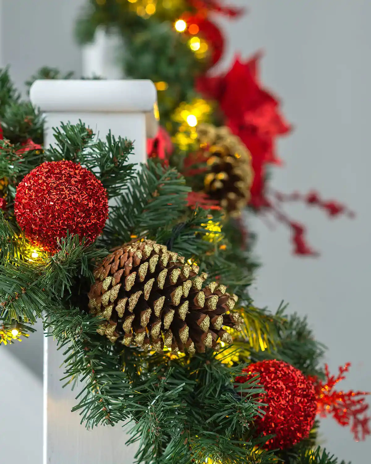 Close-up of red decorated Christmas garland with glitter baubles, pinecone detail and warm white LED lights
