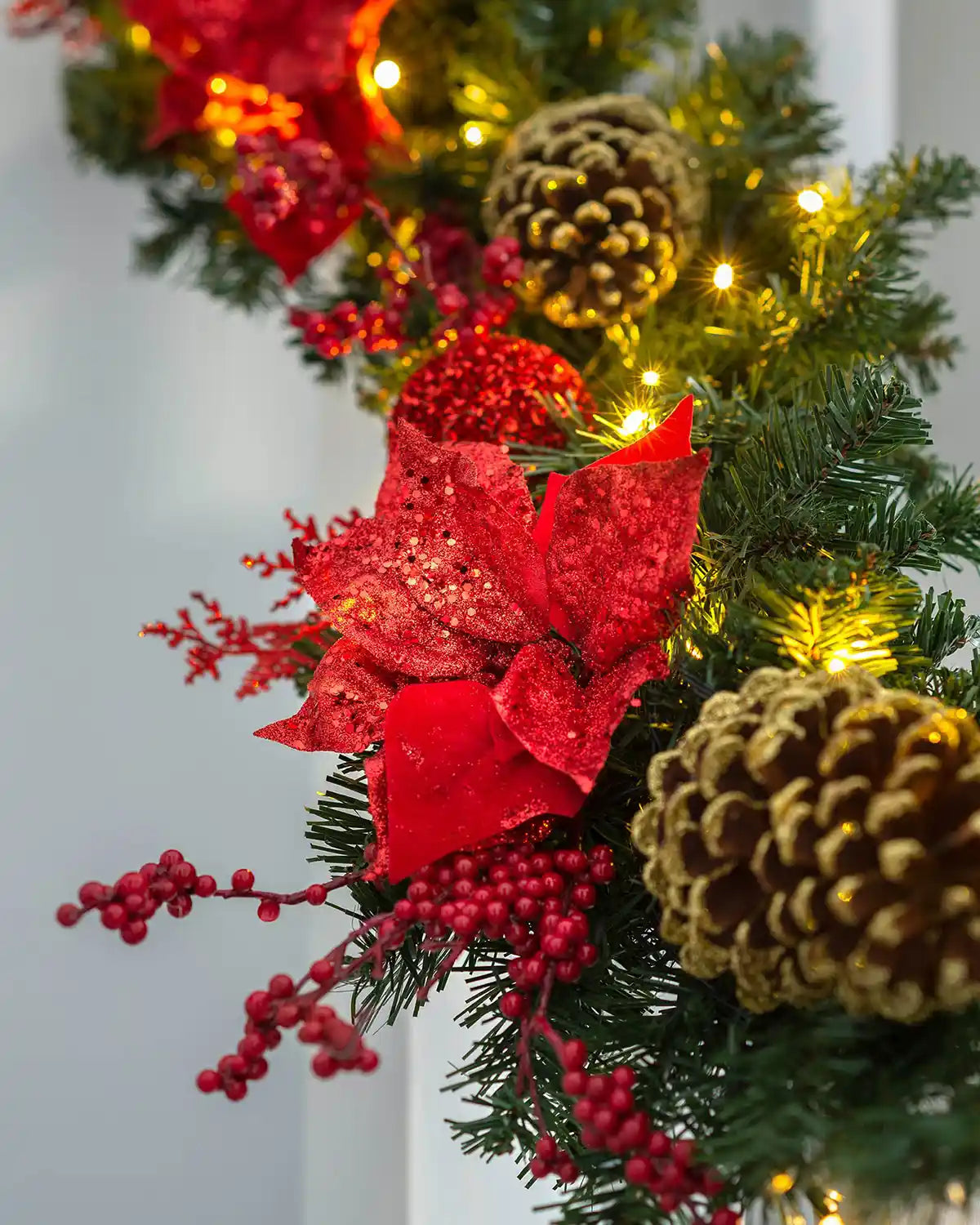 Detail close-up of red poinsettia, berries, pinecones and warm white lights on a decorated Christmas garland