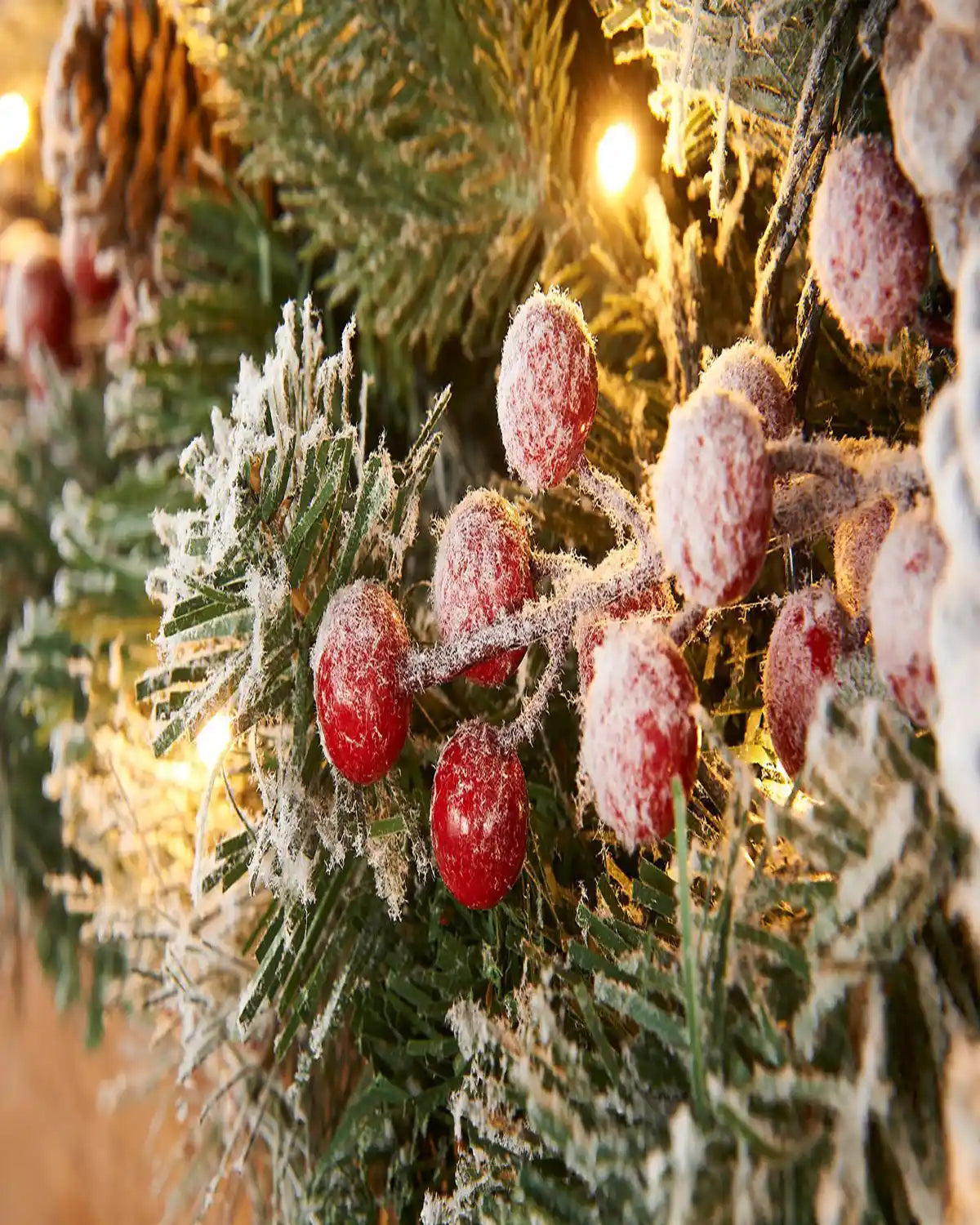 Detail close-up of frosted red berries, snowy foliage and warm white lights on a Christmas garland