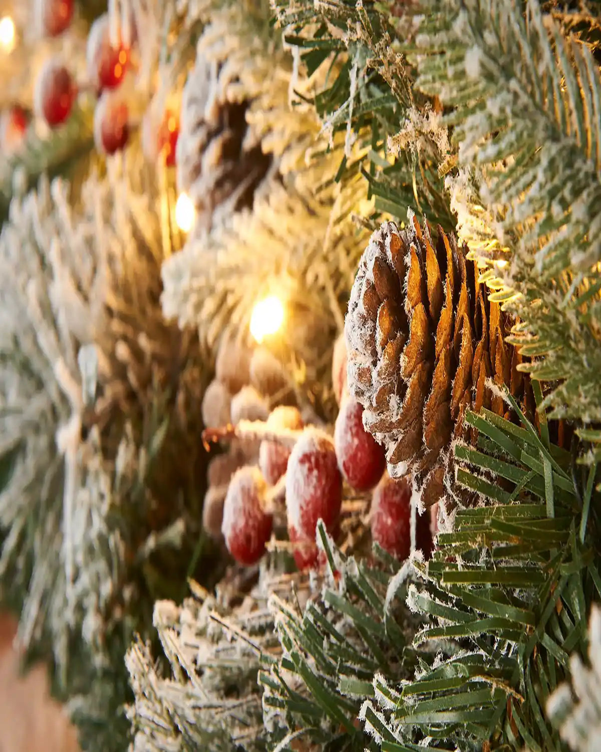 Close-up of snow flocked mixed pine garland with pinecones, frosted berries and warm white LED lights