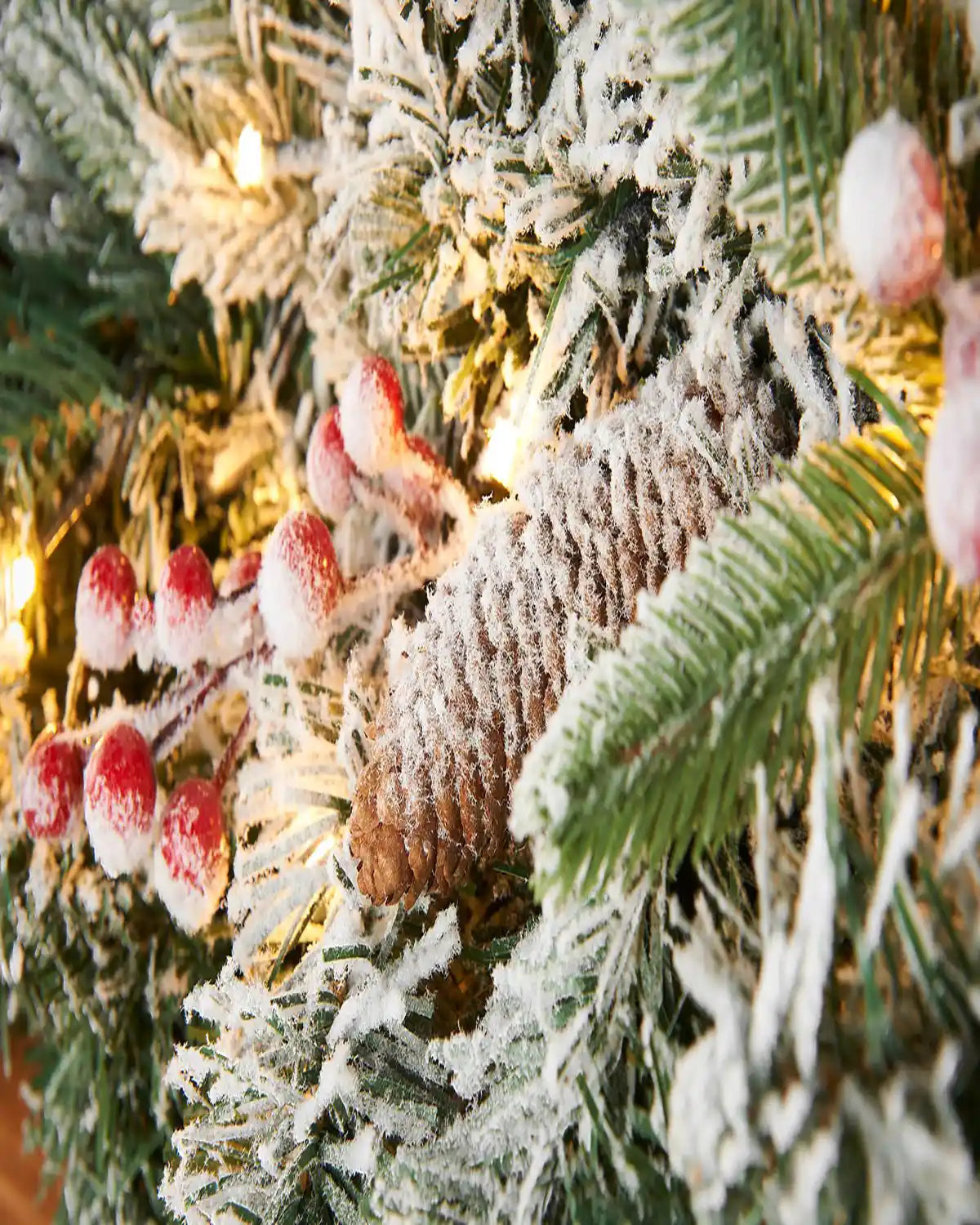 Close-up of snow flocked pinecone, frosted greenery and warm white LEDs on a mixed pine garland