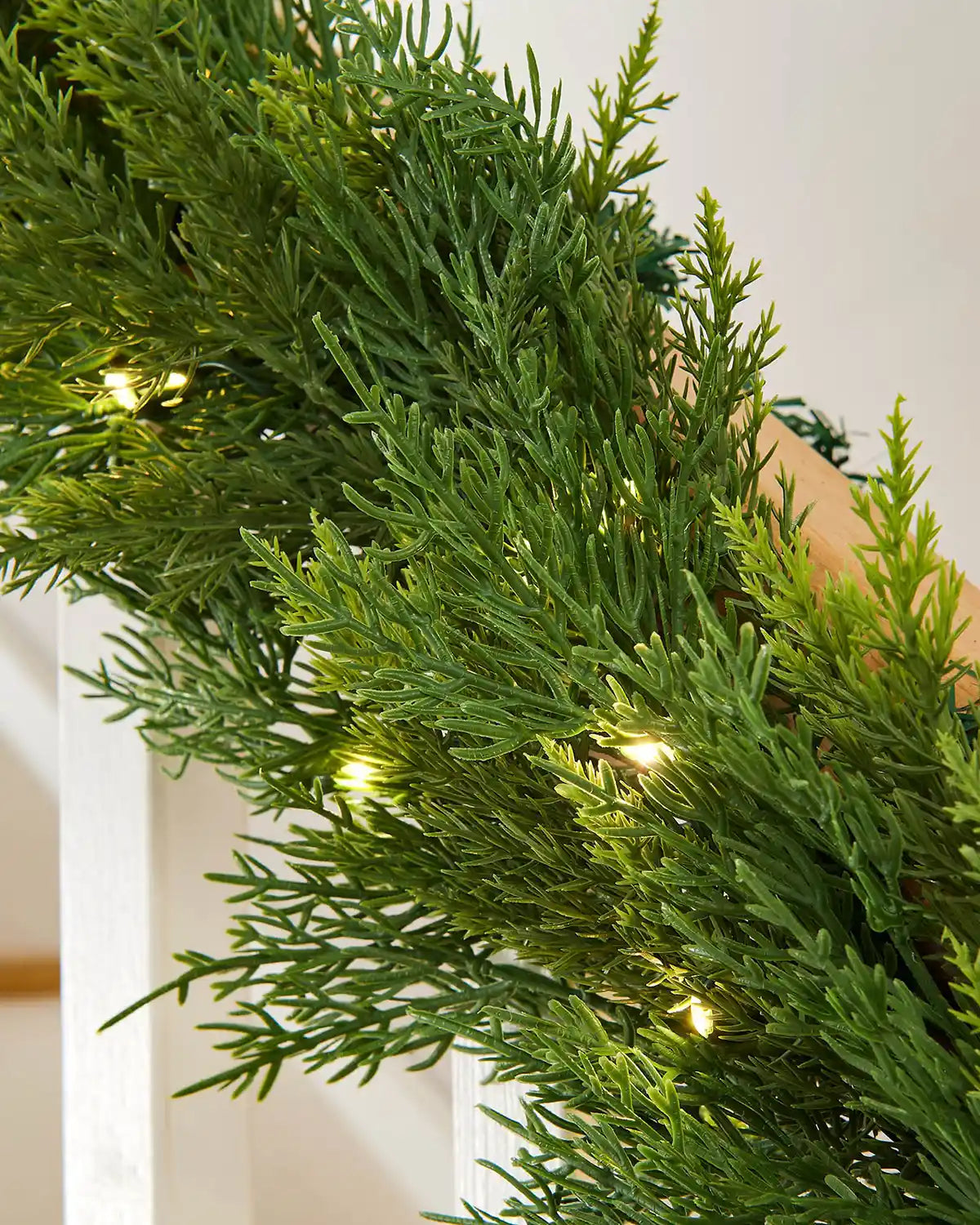 Close-up of 9ft pre-lit cypress fir garland with warm white light setting resting on wooden staircase banister 