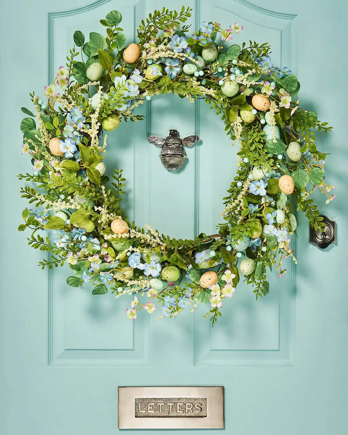 A Blue 28 inch Artificial Floral Egg Spring Wreath on a Turquoise door.